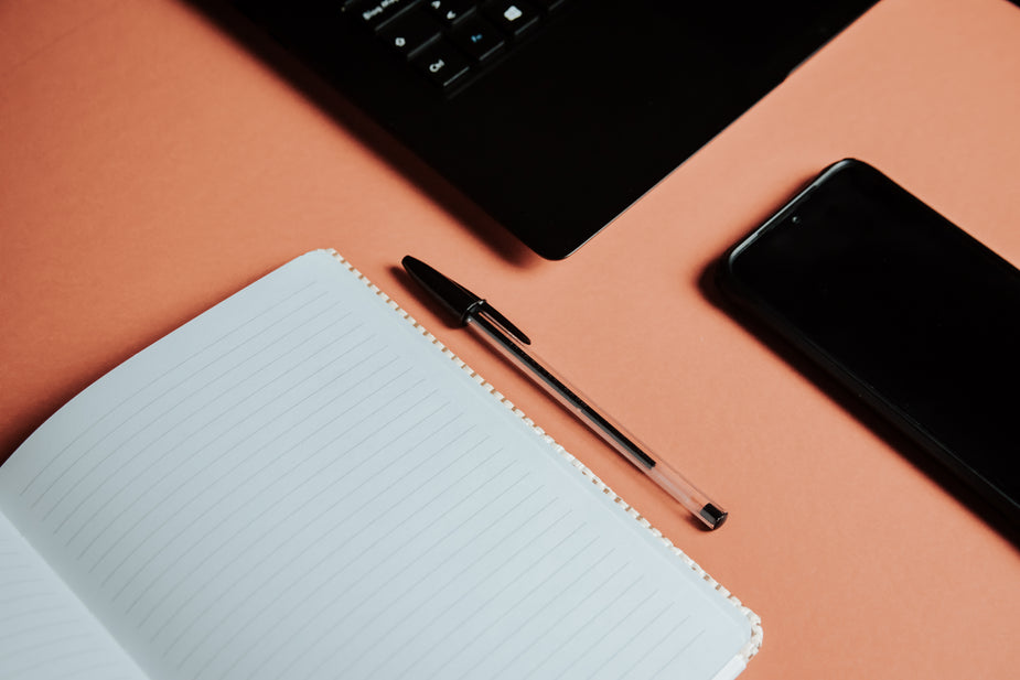 flatlay of organized pen paper laptop and cellphone