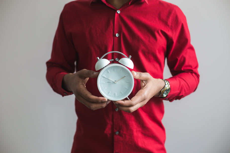 The torso and hands of a person wearing a red shirt, holding an alarm clock to manage time