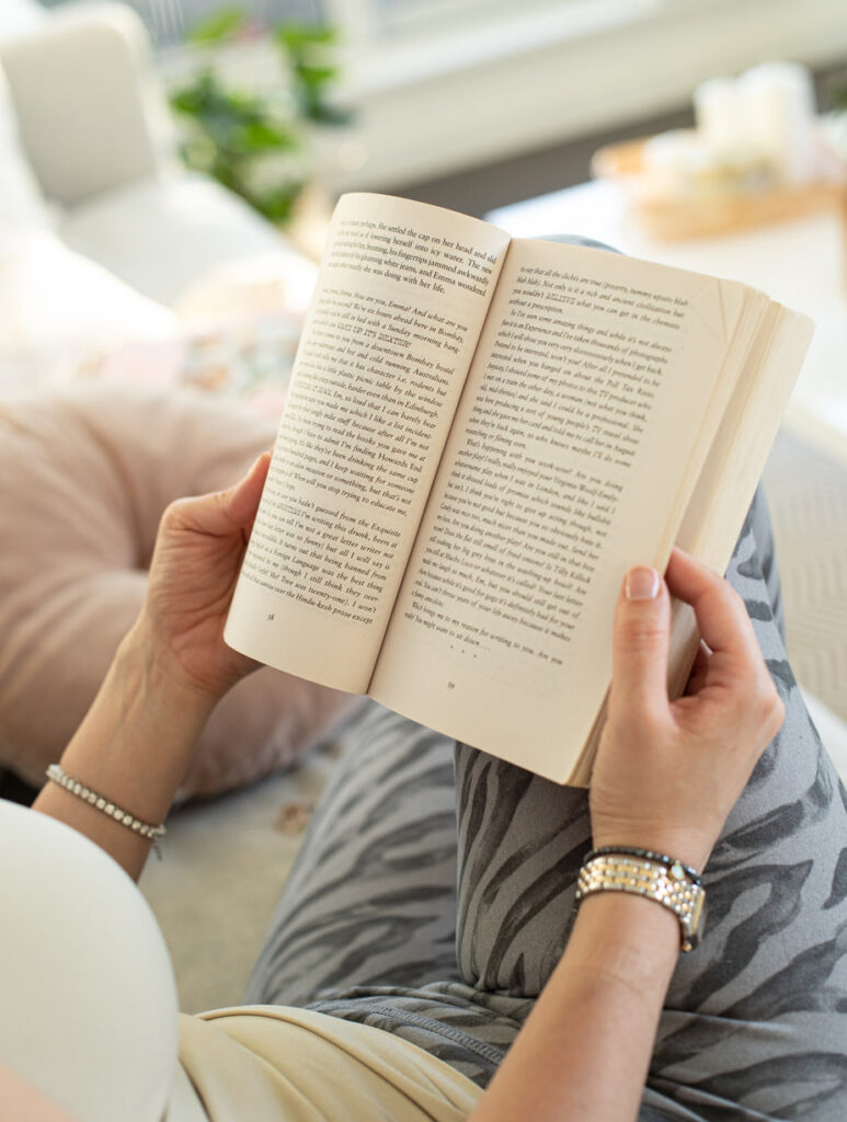 Photo of hands holding a novel open against a persons legs.