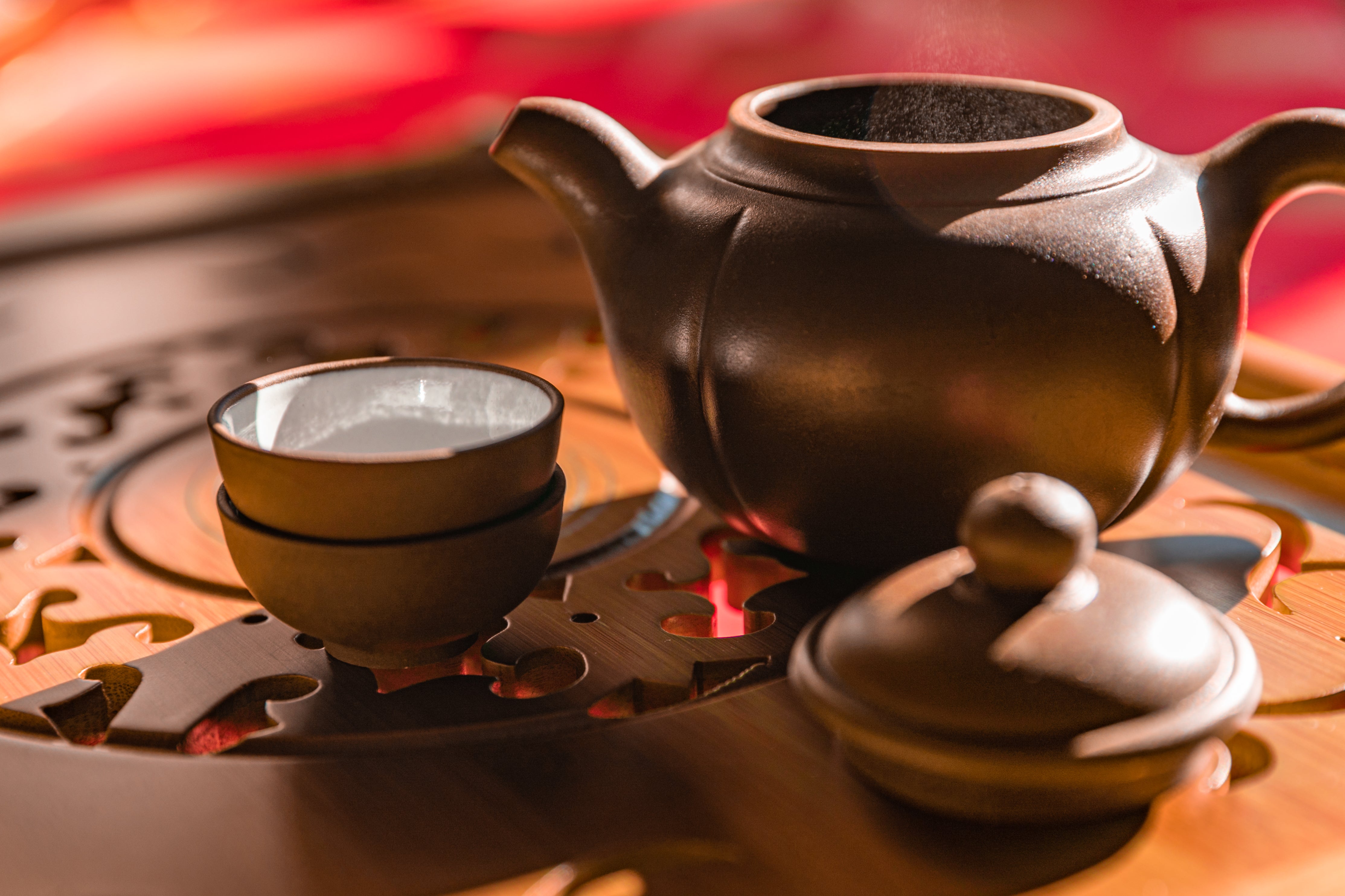 A tea pot sitting on an intricate wooden table with two cups.