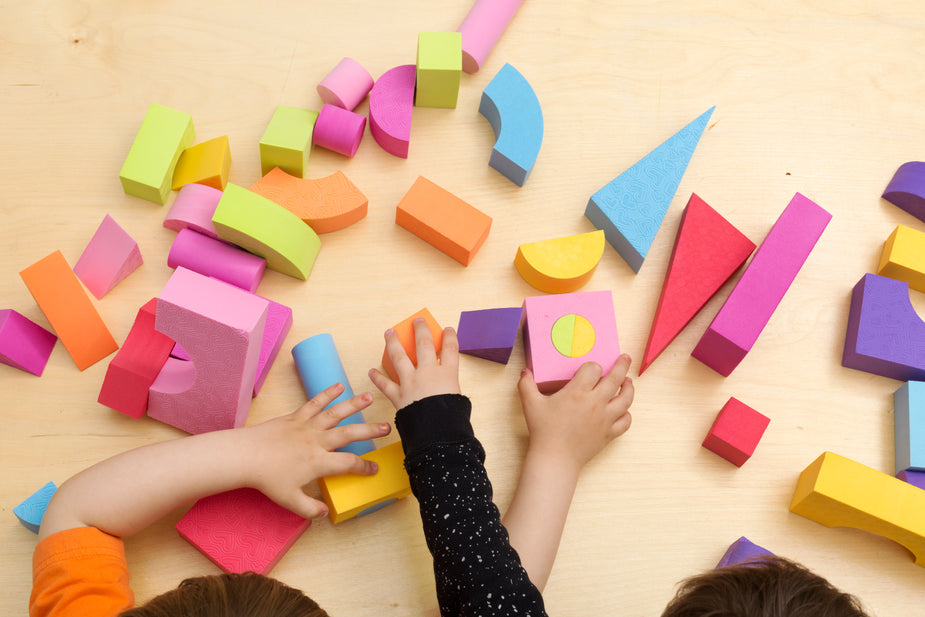 Two toddlers play together and share the colorful toys laid out before them