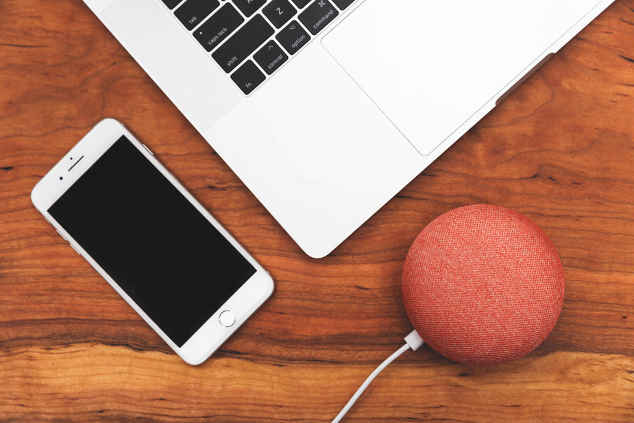 A flatlay of a living room table. Complete with a mobile phone, laptop, and smart home device.