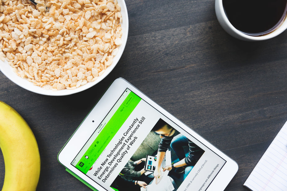 A kitchen table that's adorned with all the essentials for breakfast: a bowl of cereal, a banana, a cup of coffee, and of course, a tablet with a blog post open and ready for reading.