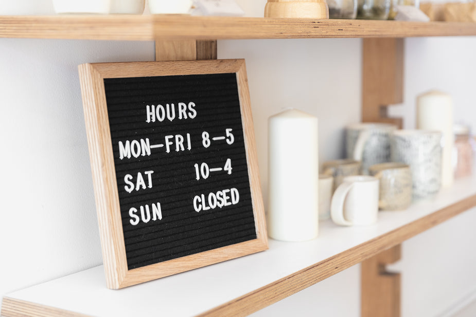 The opening hours of a store are displayed on a blackboard, which sits neatly among the pale cups and jugs on a shelf.