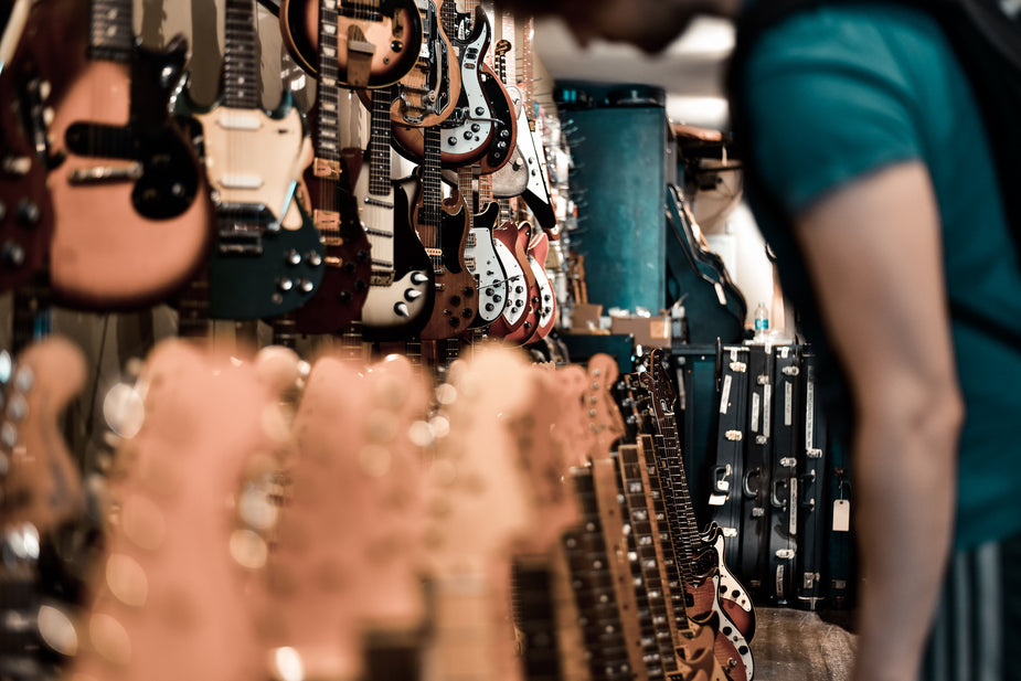 Racks of electric guitars line the walls of a local guitar shop. A man stands in the aisle browsing the selection.