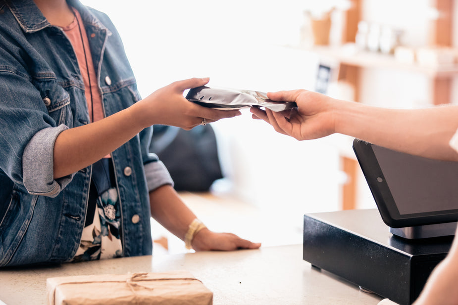 A man hands the newly purchased coffee package to his customer, wishing them a good day ahead.