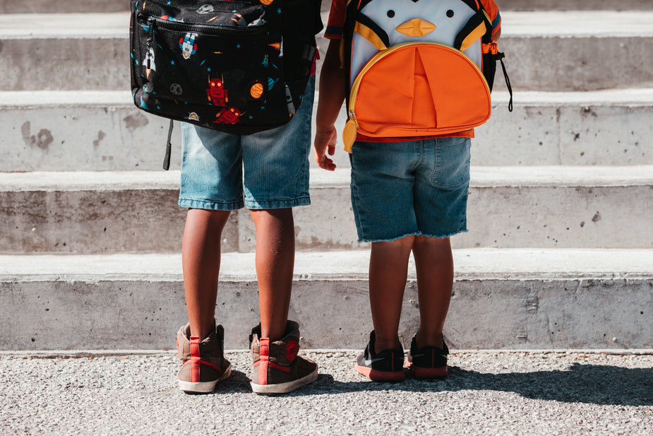 Two children stand in front of a set of steps, wearing their new school backpacks. Time to learn!