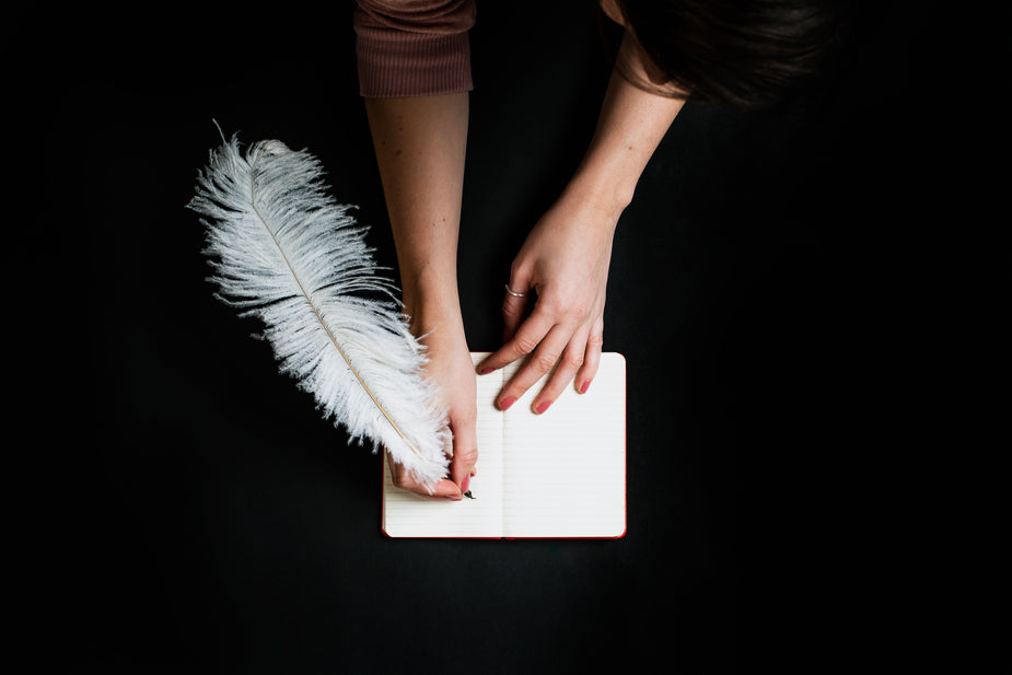 A young woman is about to write something very inspiring in her notebook using a white feather quill.