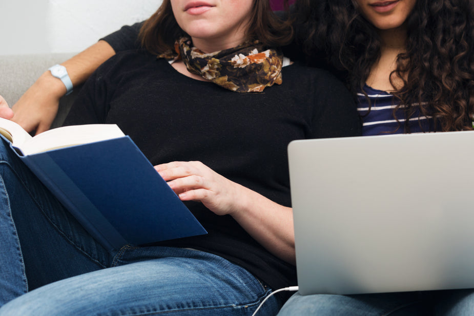 A young couple shares a relaxing moment at home. These two women know how to enjoy the finer things in life as well as their time together by reading and getting a cuddle in on the couch. Take your breaks to stay healthy while working from home