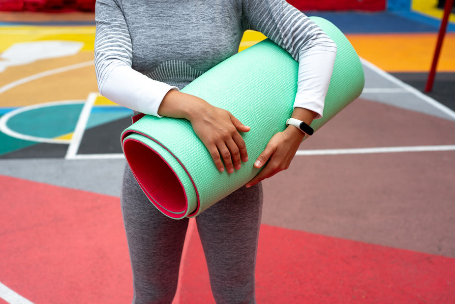 A young woman stands with a rolled up yoga matt in her hands.