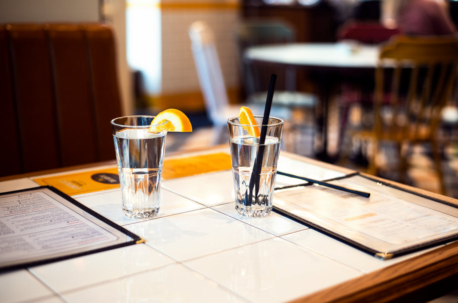 Two glasses of water with a wedge of citrus sit waiting on the table of a casual diner or restaurant.