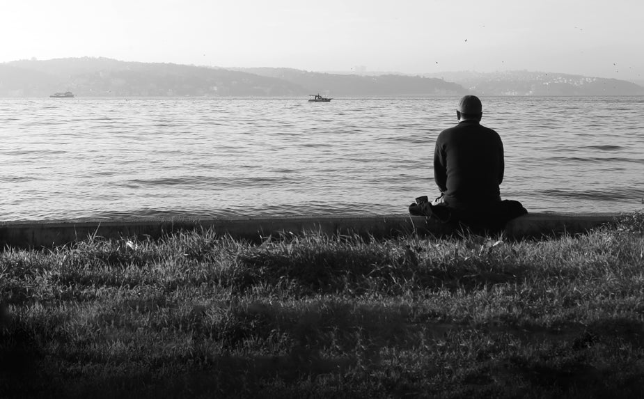 Person sits facing away from the camera towards the still water in front of them. metaphor for long term negative health effects caused by multitasking