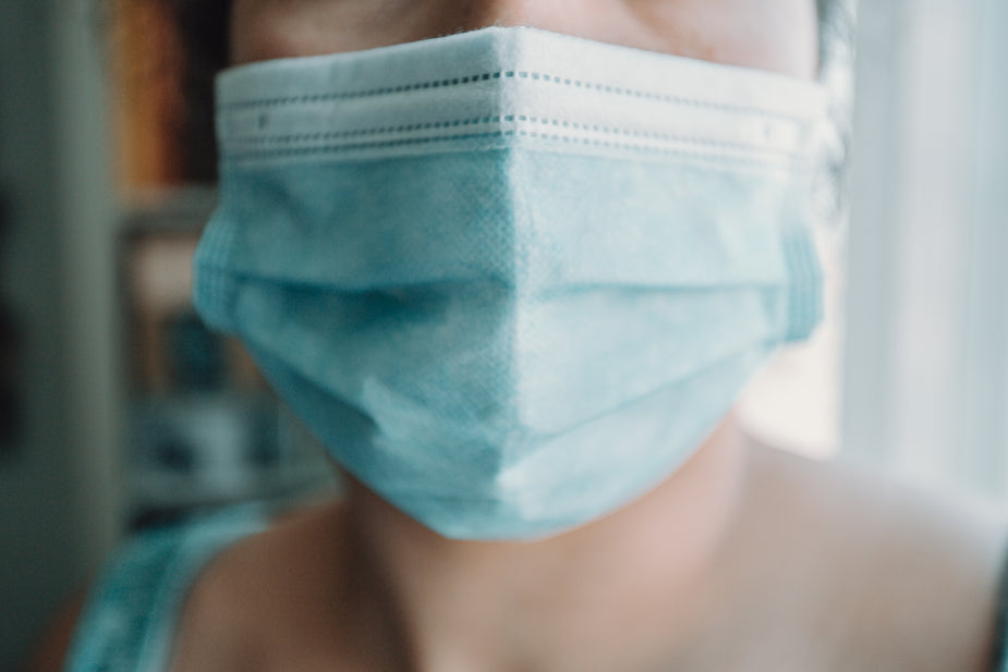 A close up of a person wearing a blue surgical face mask, protecting themselves from germs and particles. Metaphor for health issues due to lack of sleep