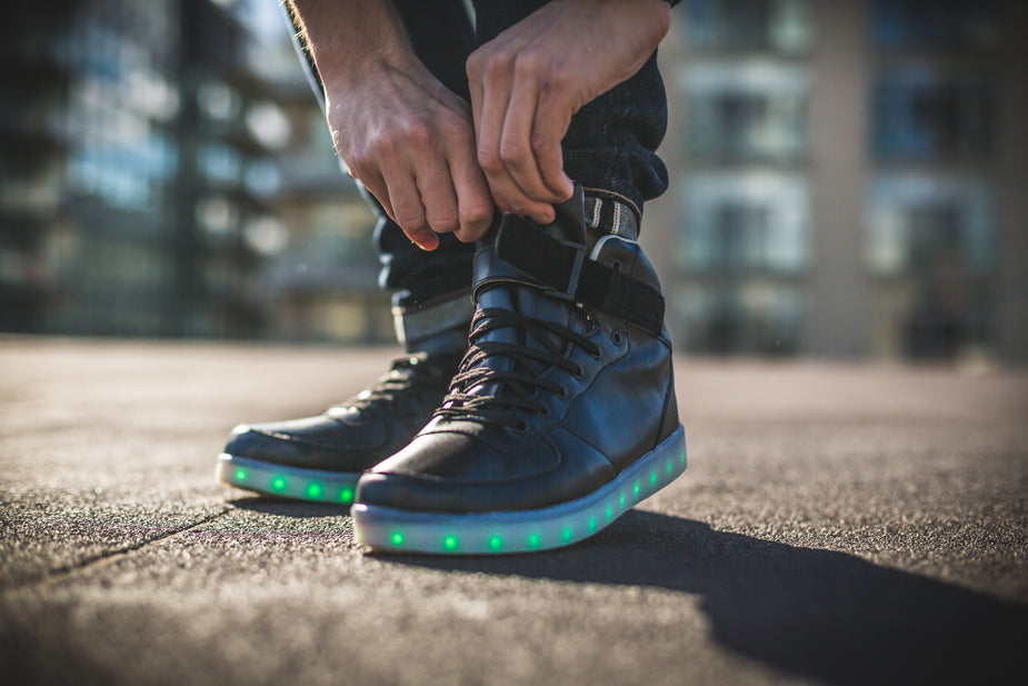 Close up of man putting black high top shoe on with green LED lights while outside. Metaphor for the misused idiom pull yourself up by your bootstraps