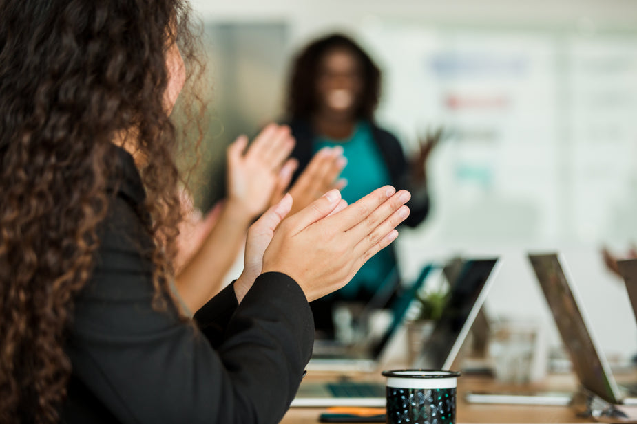 A room full of work colleagues clap their hands after a business presentation.