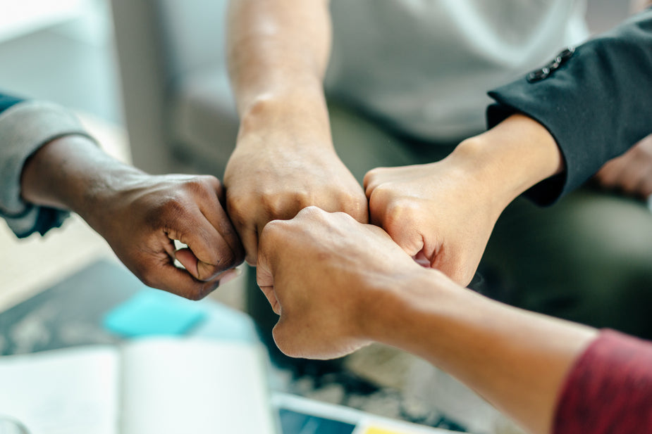 Closeup of four people bumping their fists. Metaphor for working together at Next Step Scopist