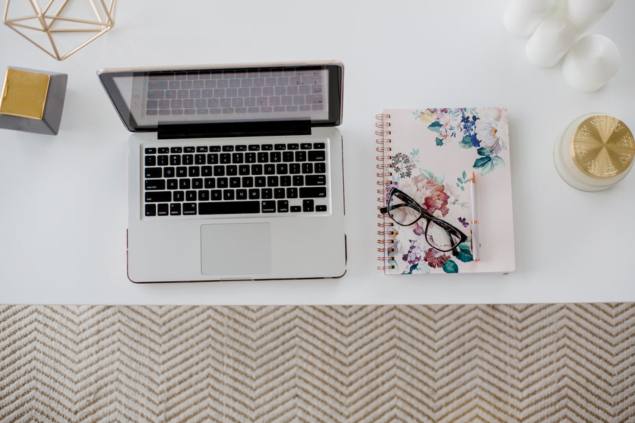 A table is topped with work day essentials, laptop, notebook, glasses and even a candle.