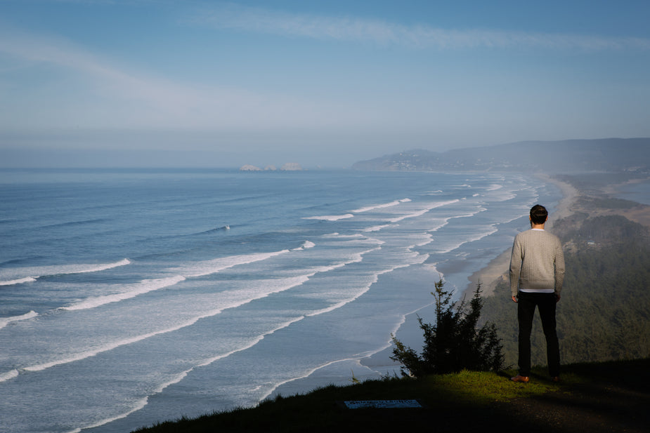 A man stands on a grassy cliffside looking out over the rolling ocean waters, capping in white as they touch the sandy beaches. what to do during a work drought and dry season