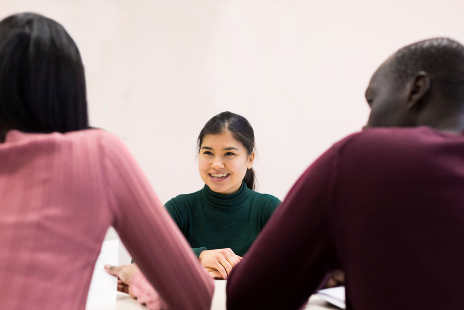 Three coworkers sit around a table for a meeting, sharing ideas and discussion about feedback