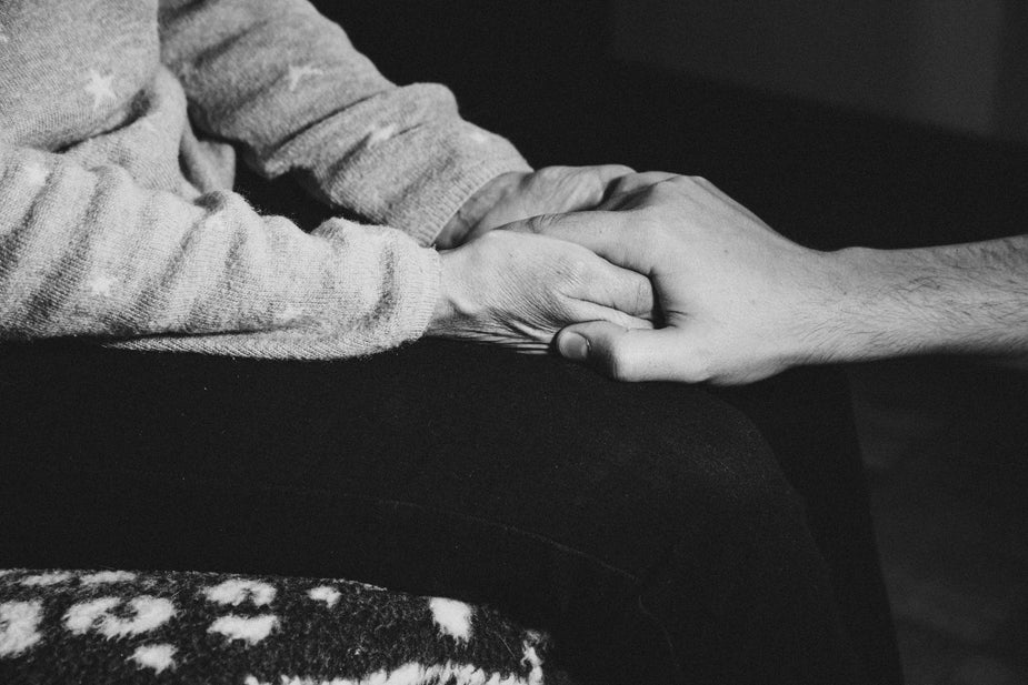 Black and white photo of a person sitting who is holding the hand of a person in front of them.