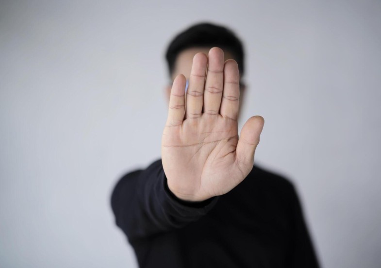 An Asian man with a beard wears a white T-shirt, stretching out his hands